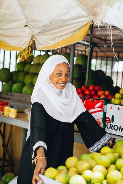 A smiling fruit seller at her stall full of oranges and watermelons