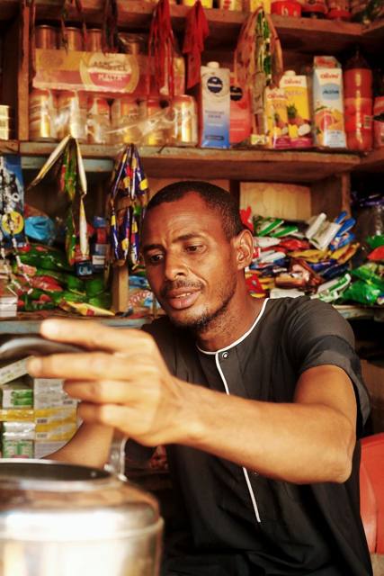 A shop owner reaching for goods on shelves full of provisions